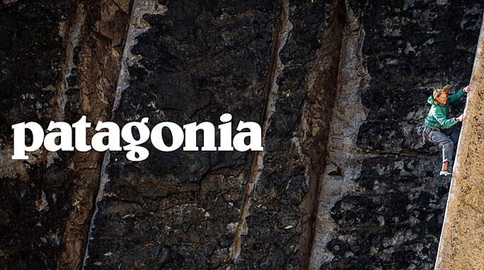 Rock climber scaling cliff next to bold Patagonia logo in print ad.