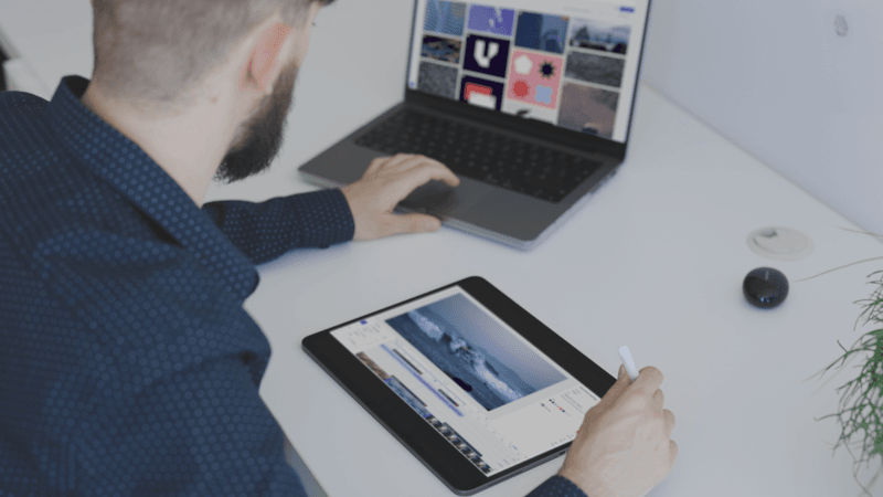 Person using a laptop and tablet to organize and review digital assets in a modern workspace.